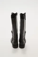 Bota alta de caña ancha color negro, con cierre lateral y detalle de hebilla ajustable en la parte superior de la caña. Suela de goma gruesa con relieve.