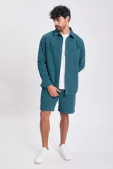 Camisa de manga larga color verde azulado, con cuello camisero, botones frontales y dos bolsillos de parche con tapa en el pecho.