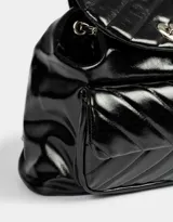 Mochila negra de cuerina acolchada con diseño de líneas diagonales. Tiene solapa con broche decorativo y botón para cerrar. Cuenta con correas regulables, manija superior de material principal y metal, y tira de ajuste de metal.