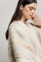 Ruana de tejido crochet color crudo con detalles de hilos de colores y flecos en el borde inferior.