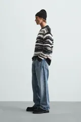 Sweater de punto con cuello redondo y manga larga, con diseño de rayas horizontales en tonos negro, gris y blanco.