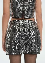 Conjunto de top corto y falda mini con lentejuelas plateadas. El top es de tirantes finos y la falda es ajustada.