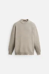Jersey de punto color beige, de corte holgado, con cuello redondo y manga larga. Tiene efecto lavado y rotos en toda la prenda.