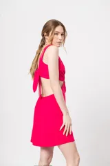 Vestido corto fucsia con escote en V y corte a la cintura. Presenta aberturas laterales y lazo ajustable en la espalda.