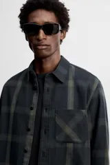 Camisa de hombre regular fit confeccionada en tejido de algodón a cuadros en tonos azul oscuro y verde oliva. Tiene cuello solapa, manga larga con puños abotonados, bolsillo de plastrón en el pecho y cierre frontal con botones.