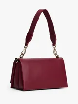Cartera rectangular de piel sintética granulada color rojo oscuro (vino/borgoña) con solapa frontal y cierre de pinza. Presenta herrajes metálicos dorados y un broche central con el monograma TH. Incluye una correa tejida ajustable y extraíble, y una correa corta adicional.