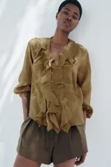 Camisa color verde oliva de tela traslúcida con escote en V, mangas largas abullonadas con puños elásticos y volantes en el frente.