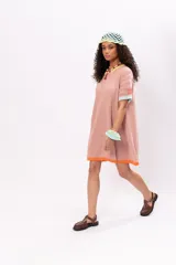 Vestido corto tipo remerón color rosa, de tejido de punto con cuello redondo y mangas cortas. Presenta ribetes en color amarillo en el cuello, celeste en las mangas y naranja en el ruedo.