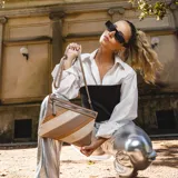 Sobre de mano de símil cuero con diseño de franjas diagonales en negro, blanco y marrón. Cuenta con cierre metálico frontal, bolsillo interior con cierre y otro abierto con división. Incluye correa desmontable para usar como bandolera.