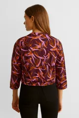 Campera bomber manga larga con estampado de hojas en tonos naranja y rosa sobre fondo borgoña, con cierre frontal y cuello redondo.