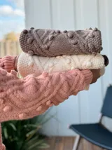 Sweater tejido grueso color rosa, con cuello alto, mangas largas y diseño trenzado con detalles de pompones.