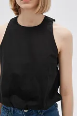 Blusa blanca de algodón sin mangas, con cuello a la base, abertura en la espalda y lazo ajustable.