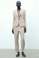 Blazer color beige de corte entallado, con cuello solapa y mangas largas. Tiene bolsillos con solapa en la parte delantera y cierre cruzado con botones.