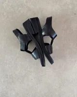 Sandalias de cuero color marrón con suela de goma negra, tiras anchas y hebilla metálica.