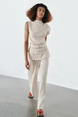 Top de algodón color beige, con cuello recto, mangas asimétricas y detalle de tejido drapeado en el lateral.