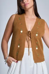 Chaleco tejido color crema con escote en V y cierre frontal con lazos. Presenta bordados de flores en tonos naranja, verde y blanco.