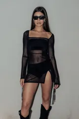 Minivestido negro de tul transparente con mangas largas acampanadas, escote cuadrado y abertura lateral con lazos. Incluye top y short de lycra negros.