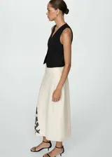Falda midi color crema, de tiro alto y corte recto. Presenta bordado de flores negras en el lateral inferior.