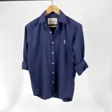 Camisa azul marino de algodón con cuello italiano, manga larga con puños abotonados y cierre frontal con botones blancos. Tiene un logo bordado en blanco en el pecho.