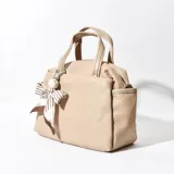 Cartera de color beige, con textura similar al cuero y lazo decorativo.