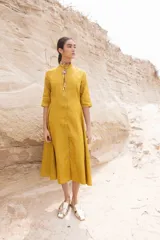 Vestido midi color mostaza, estilo camisero, con cuello mao, mangas 3/4 y cinturón trenzado.
