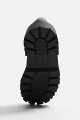 Mocasín negro de cuero con antifaz y flecos con puntas metálicas en el empeine, horma cuadrada y suela con volumen.