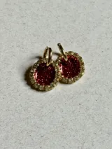 Par de aros colgantes con dije circular de resina color rojo con glitter y borde de strass. El arito es de acero quirúrgico dorado.
