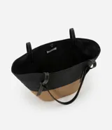 Bolso de playa grande de paja bicolor, negro en la parte superior y beige en la inferior, con asas de cuero sintético negro.