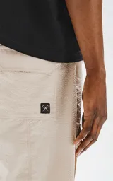 Bermuda color beige de calce relax-fit, con cintura elástica y cordón de ajuste negro. Presenta grandes bolsillos cargo con fuelle en las piernas y un cinturón de cinta negra con hebilla de plástico.