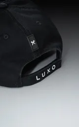 Gorra de gabardina negra con visera curva y bordado frontal en hilo rojo con la palabra "Ravers" en tipografía cursiva. Posee ajuste trasero de velcro.