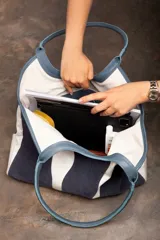 Bolso tipo tote de cuero y gamuza azul con diseño de ondas blancas. Tiene doble asa de cuero azul y base de cuero graneado. El exterior es de gamuza y tela 100% algodón.