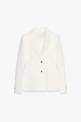 Blazer color blanco confeccionado en algodón, con cuello solapa de muescas y manga larga. Tiene bolsillos con solapa en delantero, forro interior a tono y cierre frontal con botones metálicos en relieve.