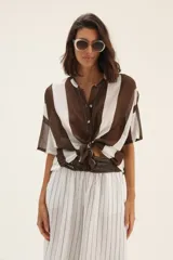 Camisa marrón y blanca a rayas verticales, con cuello mao y mangas cortas. Se ata en la parte delantera.