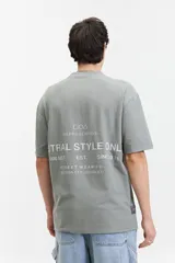 Remera de manga corta color verde grisáceo, corte oversize con cuello redondo y estampado con la frase 'STRAL STYLE ONL' en la espalda.