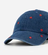 Gorra de béisbol de denim azul, con visera curva y bordados pequeños de corazones rojos.