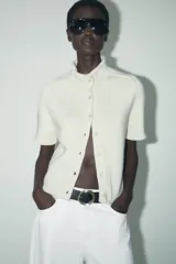 Chaqueta color blanco de tejido de punto, con cuello mao, manga corta y cierre frontal con botones.