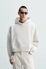 Sudadera con capucha color crudo, corte boxy, manga larga y bolsillo tipo canguro.