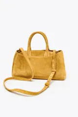 Bolso mini city color mostaza de serraje, con asa de mano y asa bandolera extraíble. Tiene un bolsillo interior con cremallera y cierre mediante botón imantado.