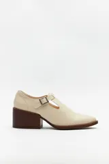 Zapato color crema con diseño tipo T-bar, tira con hebilla lateral y taco ancho de madera.