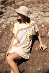 Vestido corto de algodón, con bloques de color en tonos pastel (amarillo claro, beige y rosado pálido) unidos por volados fruncidos en tonos marrón claro y amarillo. Presenta cuello redondo y mangas cortas.