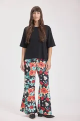 Pantalón palazzo de tela fluida con estampado floral en tonos naranja, celeste y blanco sobre fondo negro.