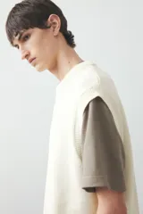Chaleco de punto color crema con cuello redondo y ribete acanalado en cuello, sisas y bajo.