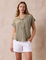 Camisa verde oliva de manga corta con cuello con solapa y abertura central con botones. Tiene un bolsillo aplicado en el pecho.