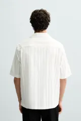 Camisa de calce relajado confeccionada en tejido jacquard de mezcla de algodón y viscosa. Presenta cuello bowling, manga corta, aberturas laterales en el bajo y cierre frontal con botones.