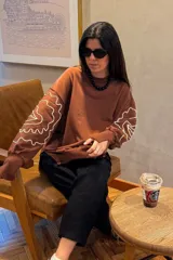 Buzo de manga larga color marrón con bordados en hilo claro de diseño abstracto/ondulado en las mangas.