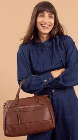 Cartera de mano o bandolera negra, de material símil cuero, con forma redondeada y base plana. Presenta dos asas cortas superiores y una correa larga ajustable para llevar al hombro. Cuenta con un bolsillo frontal con cierre metálico.