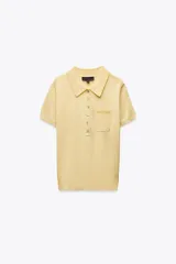 Top de punto fino color amarillo, confeccionado con lana. Tiene cuello polo, manga corta, bolsillo delantero y cierre frontal con botones.