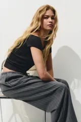 Pantalón gris oscuro a rayas verticales finas, de corte holgado, con elástico y cordón ajustable en la cintura, bolsillos laterales y bolsillos decorativos en la parte trasera. Confeccionado en sarga.