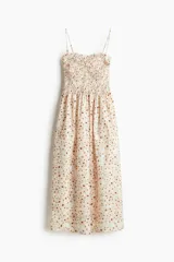 Vestido midi blanco con estampado floral en tonos naranja y marrón. Tiene breteles finos, escote recto y cuerpo fruncido con elástico en el busto.