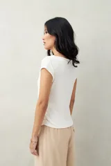Top color beige de tejido acanalado, con cuello recto, sin mangas y terminación asimétrica en pico.